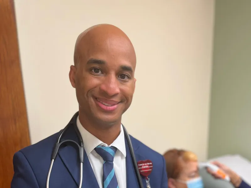 Dr. Dwayne Gordon at Post-COVID Clinic while a woman gets temperature taken in the background.